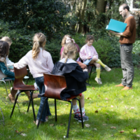 foto groep leerlingen woord zit buiten in het gras in een kring hun tekst te leren